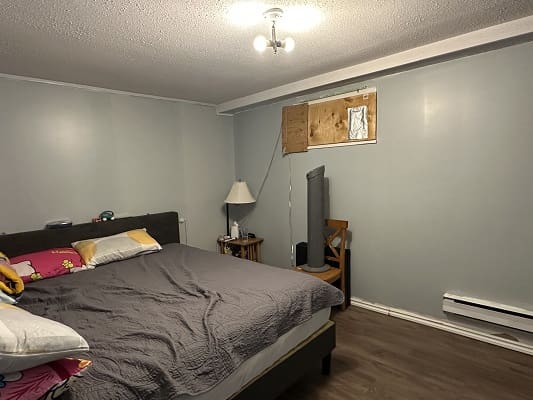 Bedroom with gray bed and boarded window.