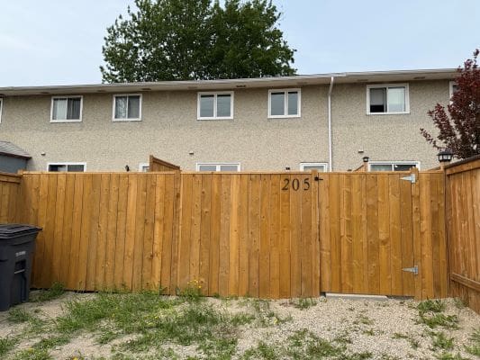 Wooden fence with house and trees behind.