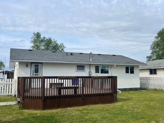 White house with wooden deck and lawn.