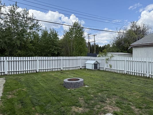 Fenced backyard with fire pit and grass.