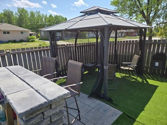 Outdoor gazebo with chairs in fenced yard.