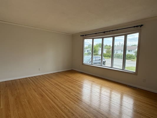 Empty room with large window and hardwood floor.