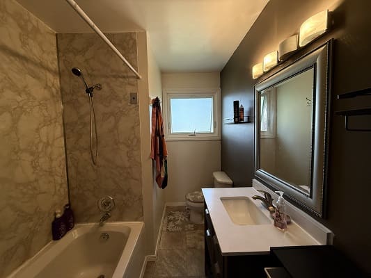 Bathroom with bathtub, sink, mirror, and window.
