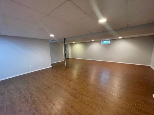 Spacious basement with wooden flooring.
