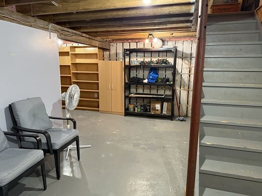 Basement with shelves, chairs, and stairs.