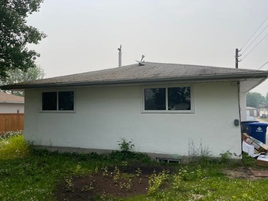 Small white house with overgrown yard.