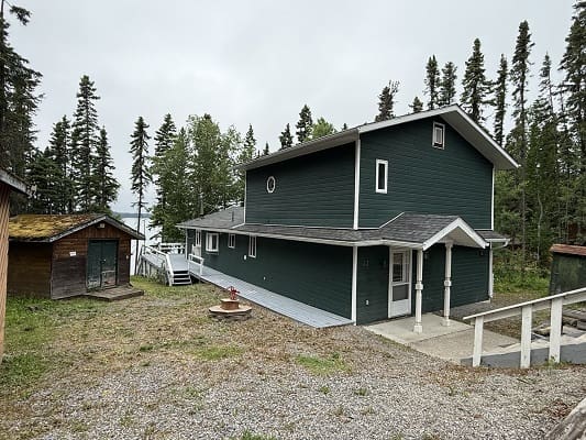 Dark green house surrounded by forest trees.