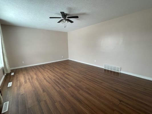 Empty room with wooden flooring and fan.