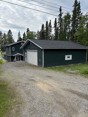 Dark green house with garage, surrounded by trees.