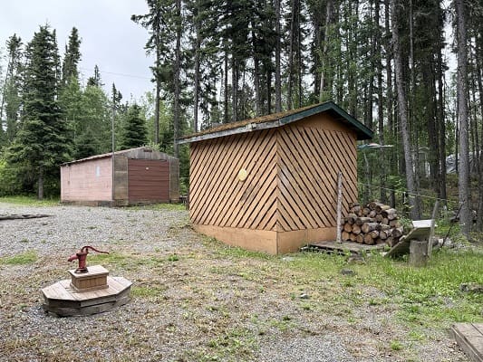 Wooden sheds surrounded by trees and logs.