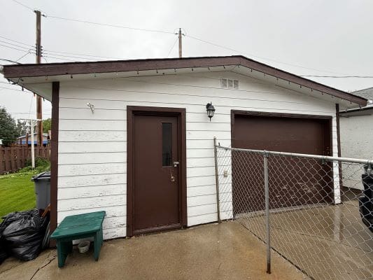 White garage with brown door and fence.