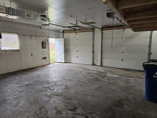 Empty garage with open door and bins.