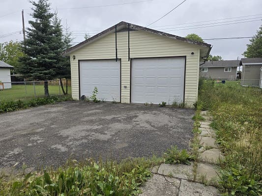 Two-car garage with overgrown driveway shrubs.