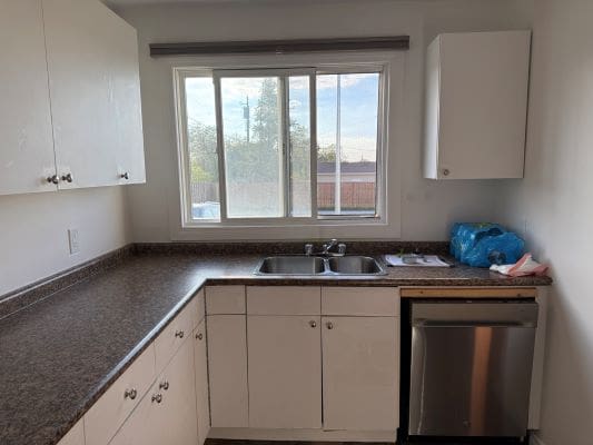 Small kitchen with white cabinets and window.