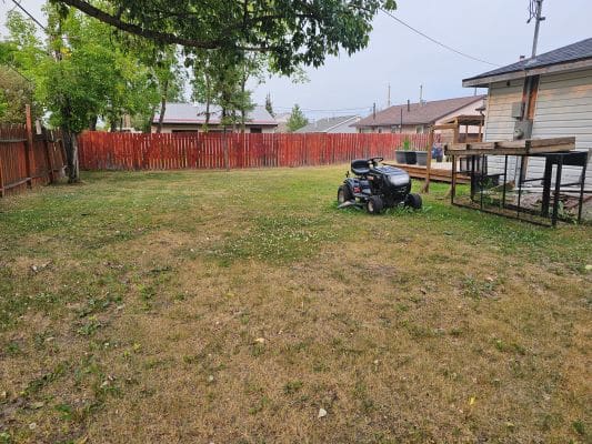 Lawn with riding mower and wooden fence.