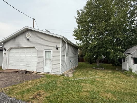Gray garage beside a large green tree.