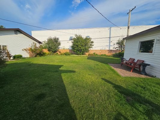 Sunny backyard with green lawn and chairs.