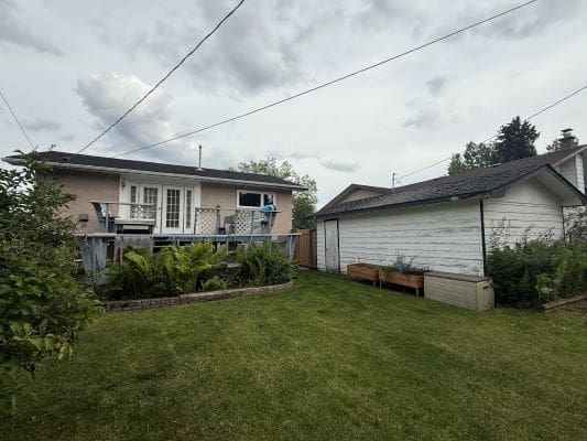 Backyard with house and garage under cloudy sky.
