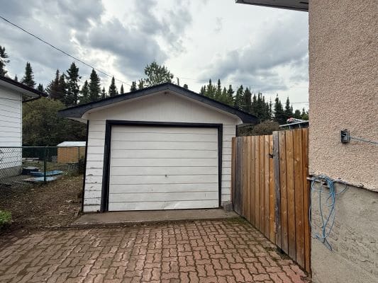 White garage with brick driveway and fence.