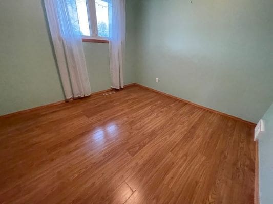 Empty room with wooden flooring and window.