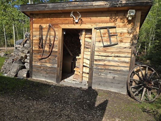 Rustic wooden shed with firewood and wagon wheel.