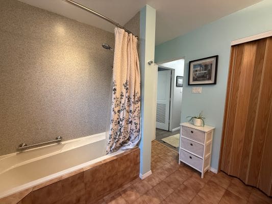 Bathroom with bathtub, shower curtain, and cabinet.