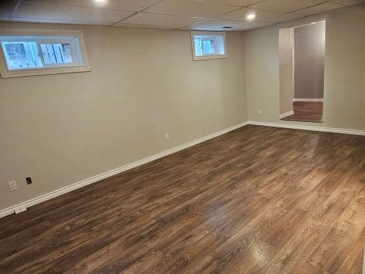 Empty basement room with wooden flooring.