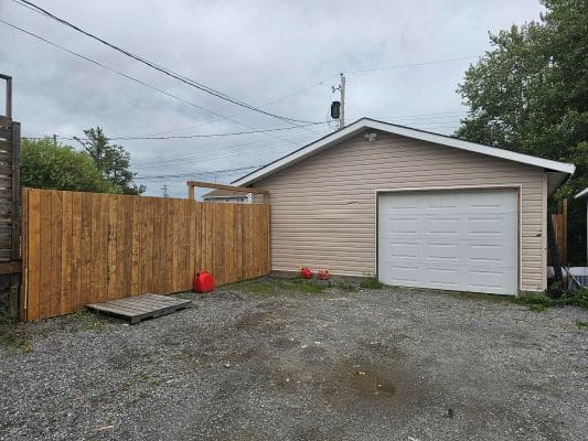 Garage with wooden fence and gravel driveway.