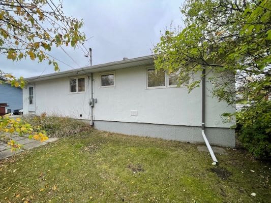 Single-story white house with surrounding greenery.