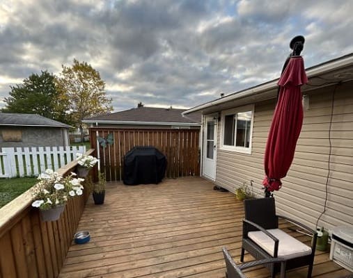 Wooden patio with chairs and red umbrella.