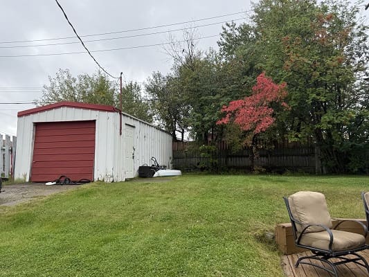 White shed with red door, grassy yard.