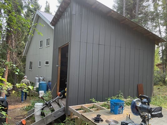 Gray shed and man in wooded area.