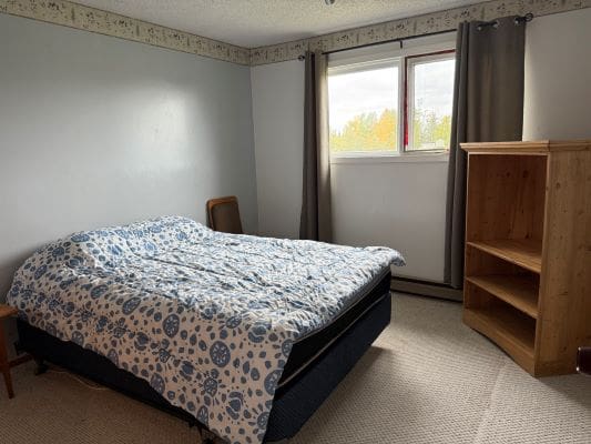 Bedroom with bed, window, and wooden shelf.