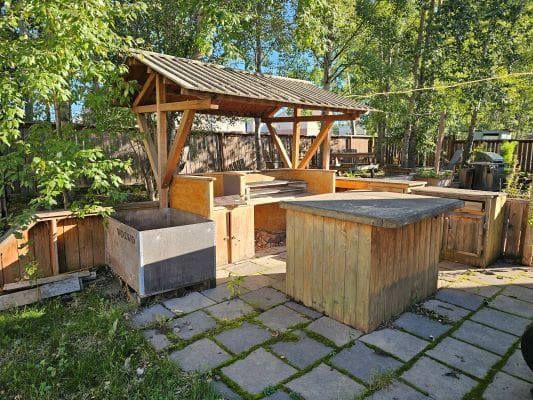 Outdoor wooden kitchen with canopy and trees.