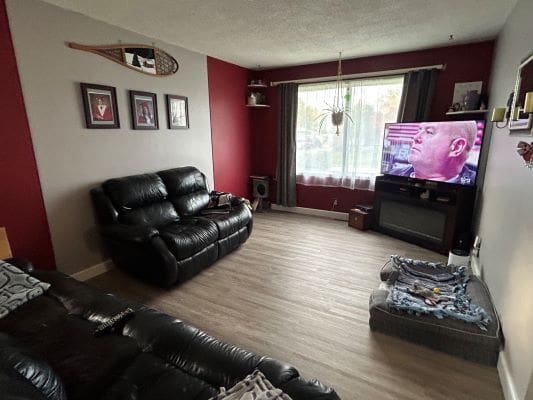 Living room with black leather sofas, TV on.