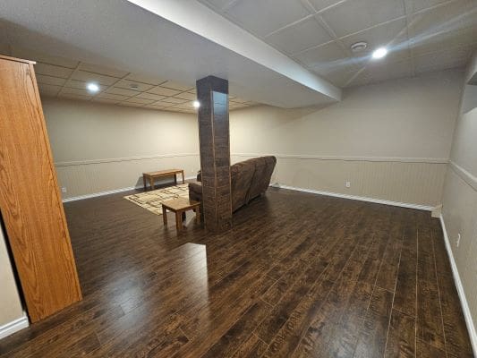 Finished basement with wooden flooring and furniture.