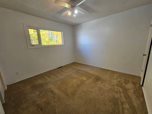 Empty room with carpet and ceiling fan.