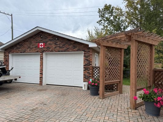 Brick garage with Canadian flag, wooden arbor.