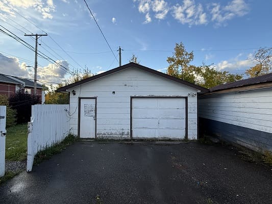 White garage with closed doors, cloudy sky.