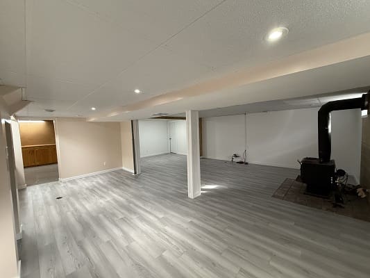 Spacious basement with wood stove and flooring.