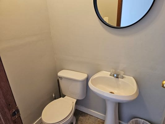 Bathroom with toilet, sink, and round mirror.