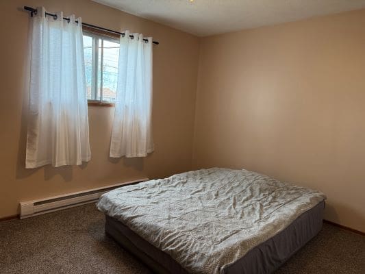 Simple bedroom with mattress and window curtains.