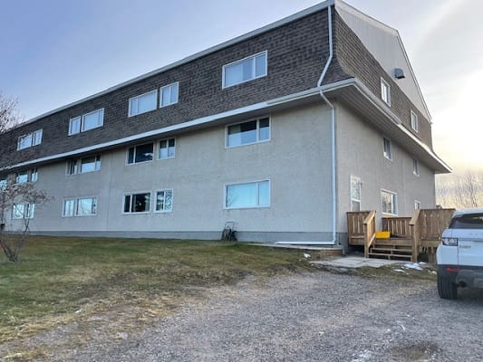 Three-story building with parked white car.