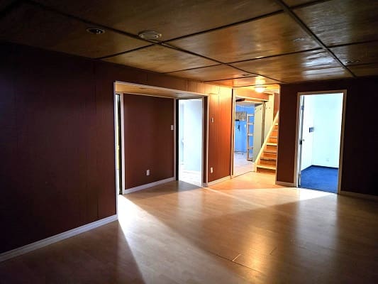 Basement room with wooden floors and stairs.