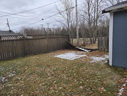 Backyard with damaged wooden fence, winter setting.