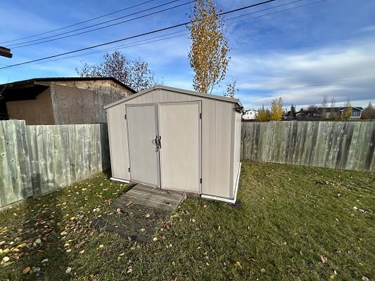 Shed in grassy backyard with wooden fence.