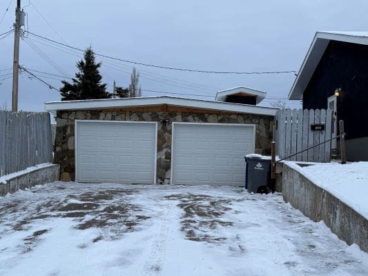 Snowy driveway leading to double garage doors.