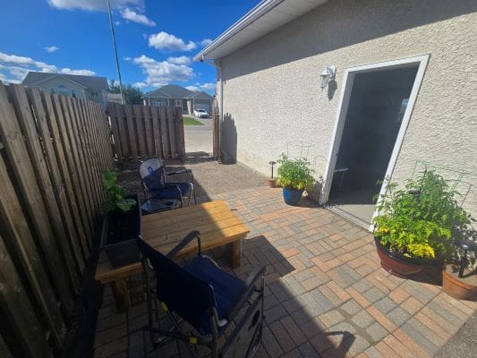 Sunny patio with chairs and potted plants.