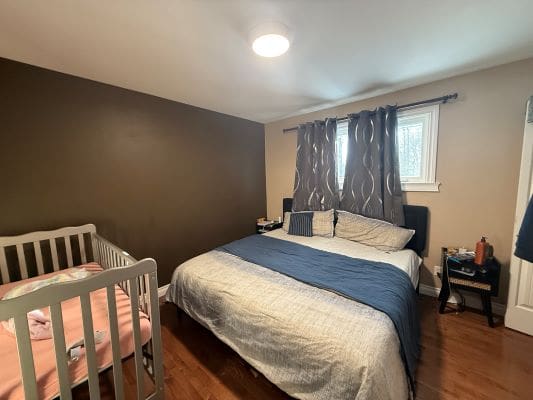 Bedroom with bed and crib, wooden floor.