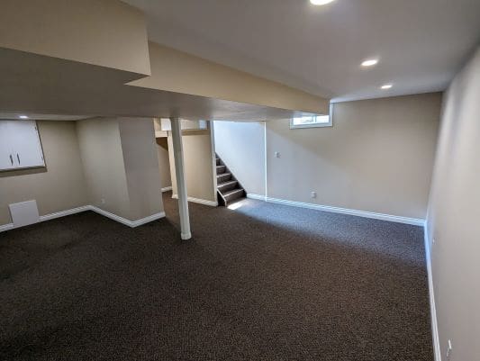Finished basement with carpet and staircase.